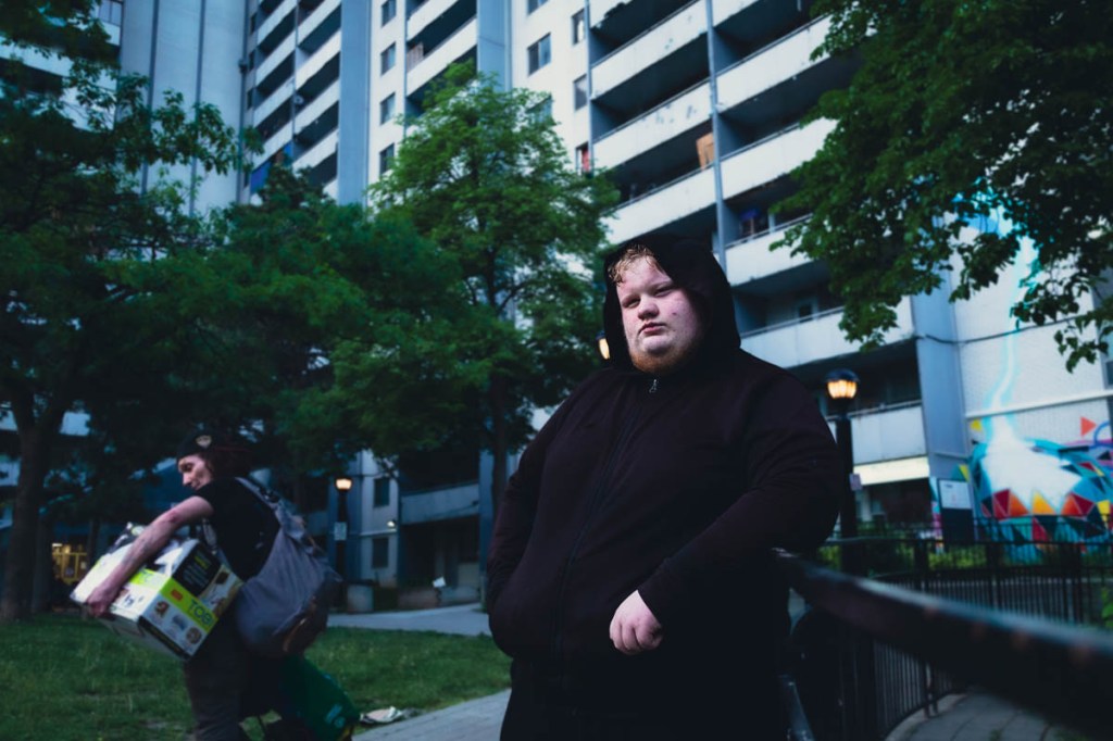 White male wearing a black hoodie leaning on a railing