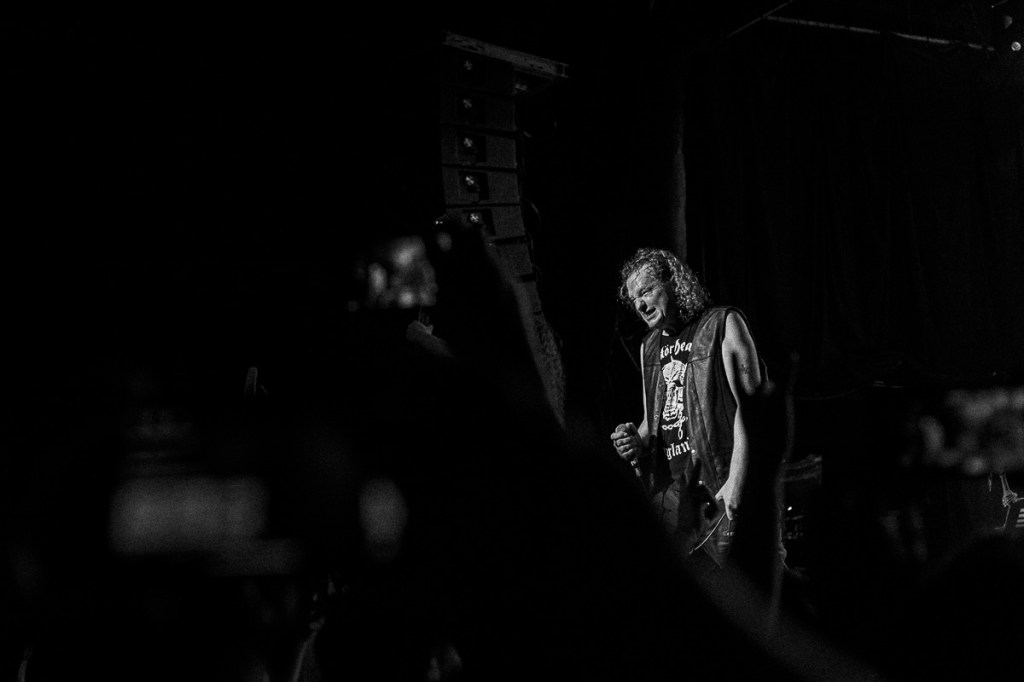 Black-and-white concert photo of heavy metal singer wearing a Motörhead shirt and leather vest.