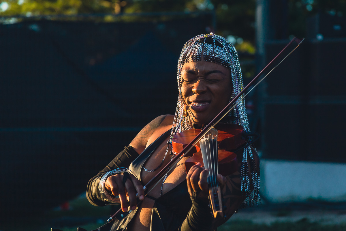 Black female artist Sudan Archives squints while playing violin as the sun sets at Luminato Festival. © Andy Lee, 2022. realandylee.com