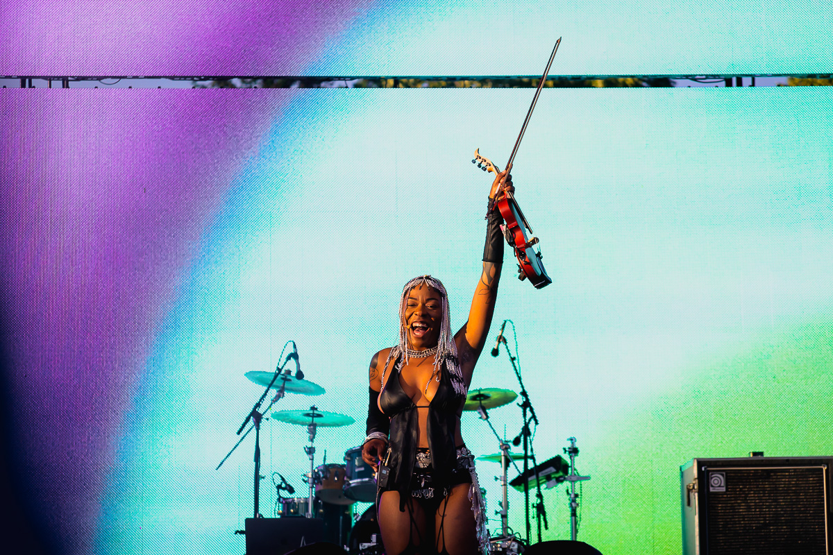 Black female artist Sudan Archives raises her violin on an outdoor stage at Luminato Festival. © Andy Lee, 2022. realandylee.com