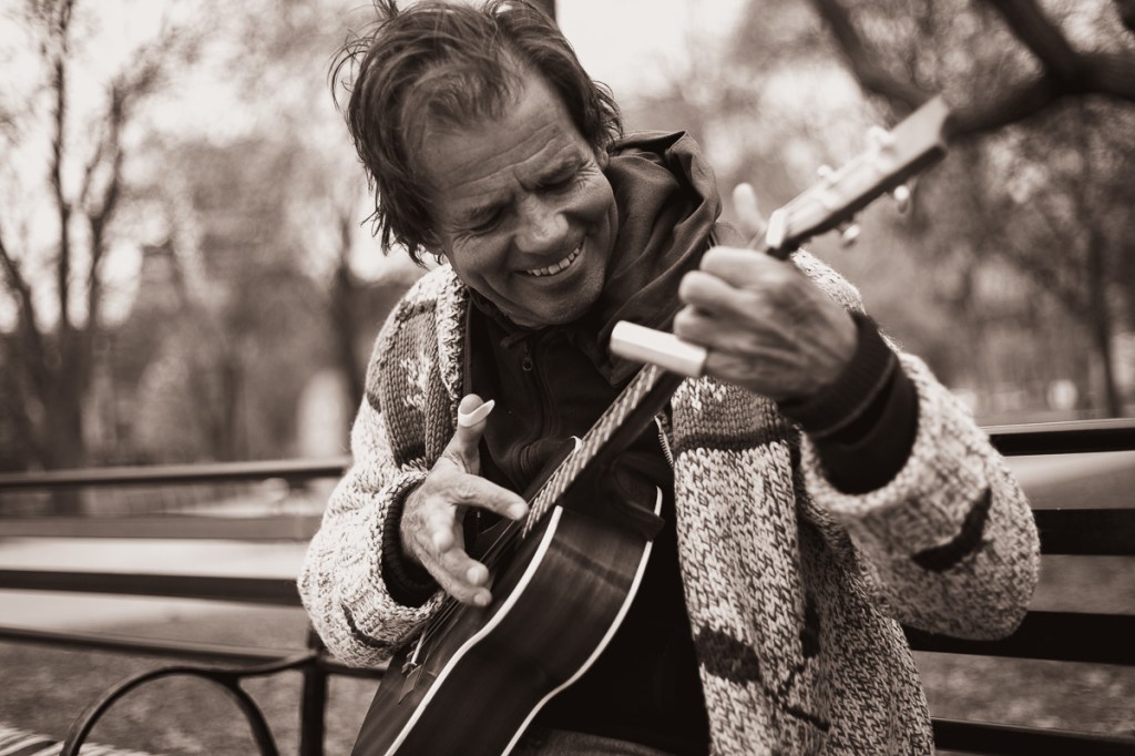 A man in a cardigan plays ukulele in on a park bench. © Andy Lee, 2022. realandylee.com