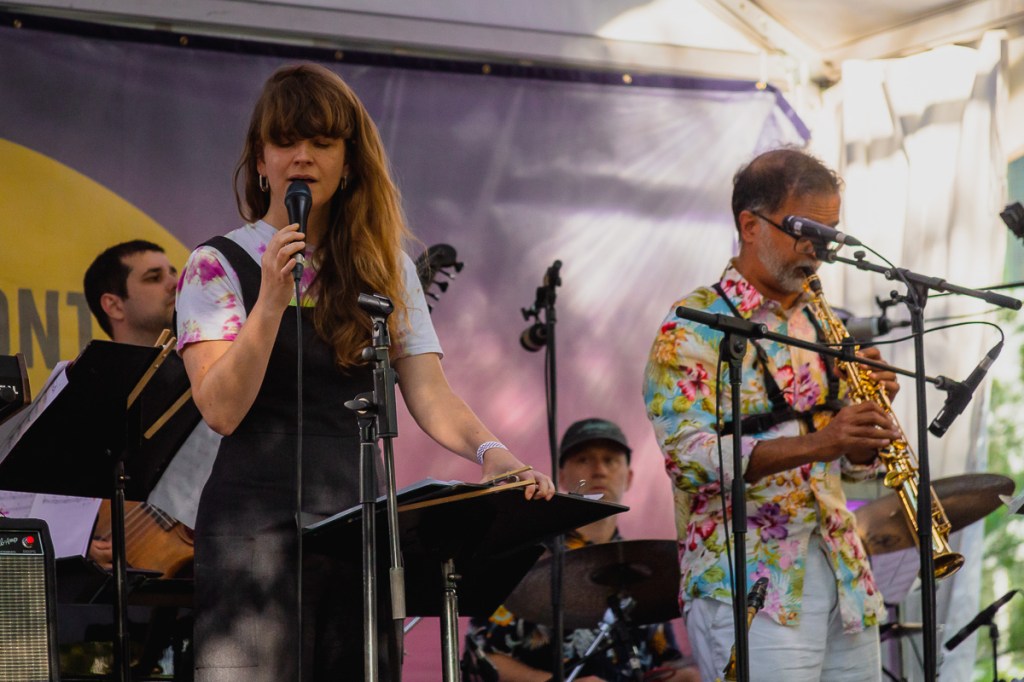 A brunette woman sings while a brown man plays soprano sax. © Andy Lee, 2022. realandylee.com