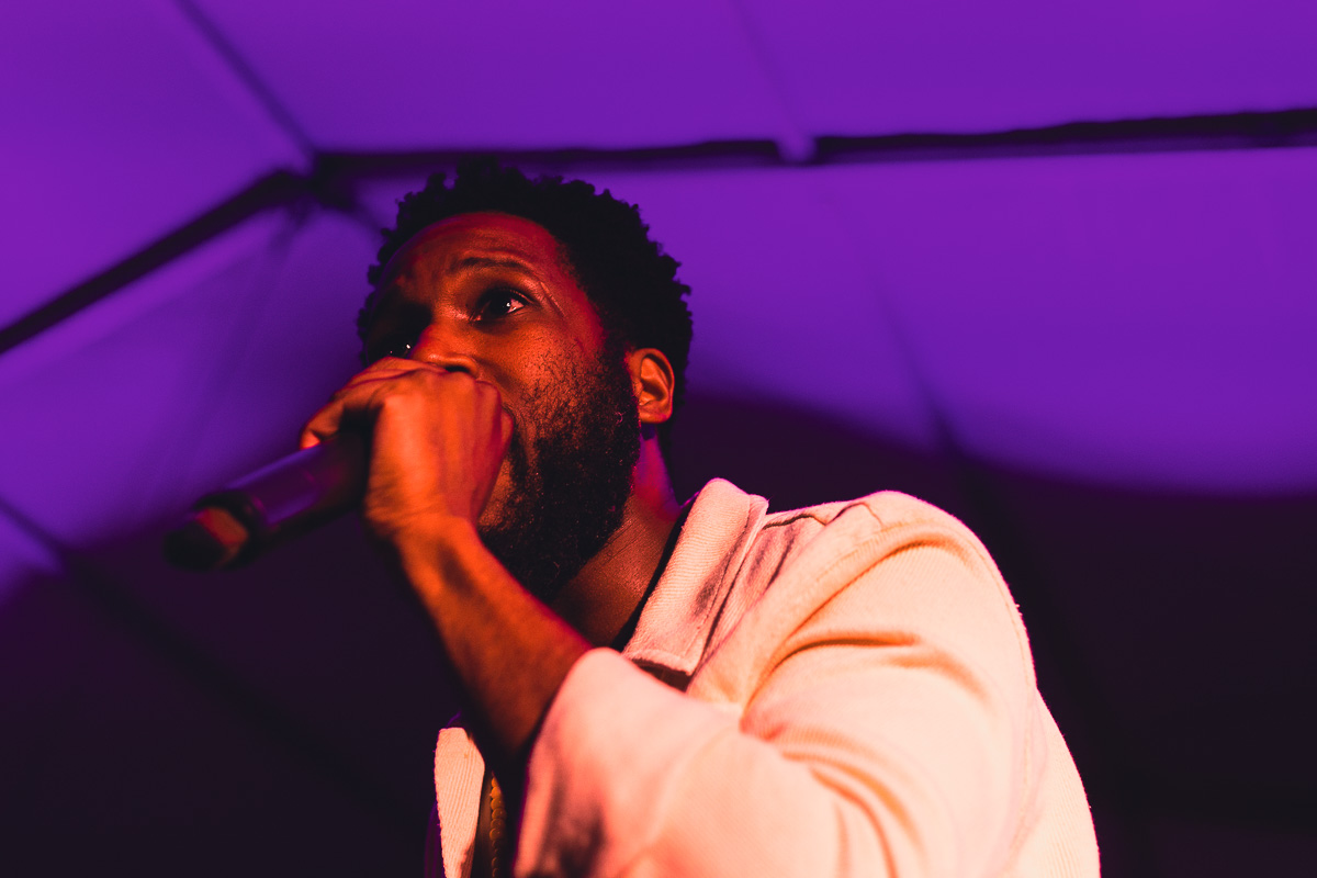 Black man singing into a microphone inside a tent with purple light. © Andy Lee, 2022. realandylee.com