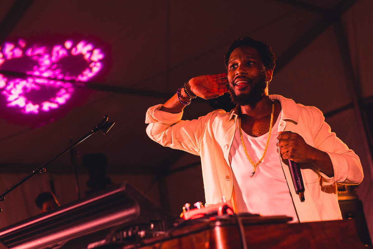 A Black man cups his ear to the crowd from inside a festival tent. © Andy Lee, 2022. realandylee.com