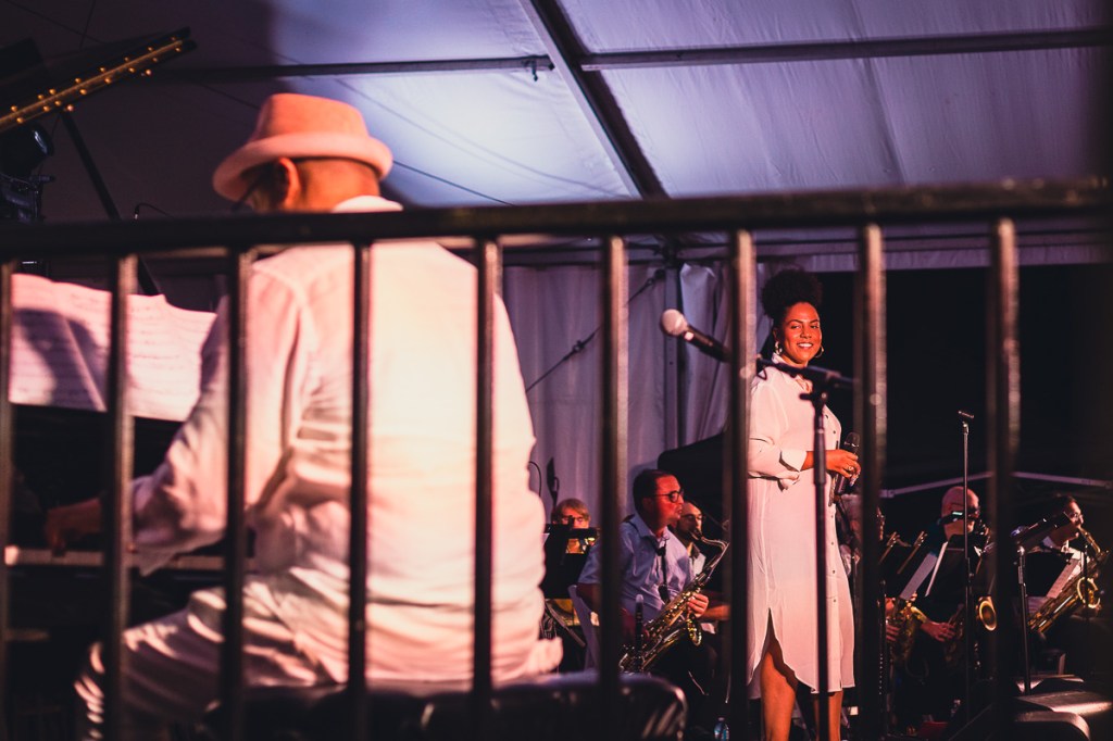 A Black woman in a white shirt dress smiles while looking at a male pianist dressed in white. © Andy Lee, 2022. realandylee.com