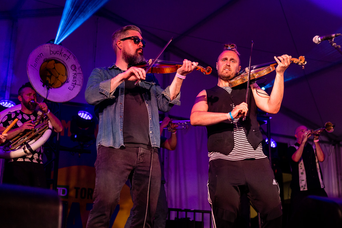 Two white men playing violin with a sousaphone player and trumpet players behind them. © Andy Lee, 2022. realandylee.com