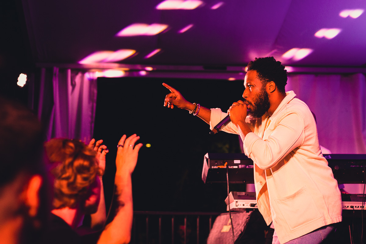 A Black man points while singing to a crowd from a festival tent. © Andy Lee, 2022. realandylee.com