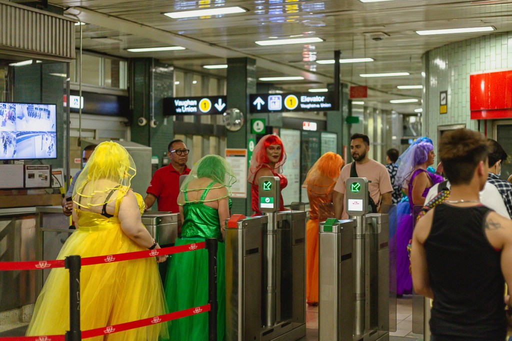 Drag queens wearing colourful dresses entering a subway station. © Andy Lee, 2022. realandylee.com