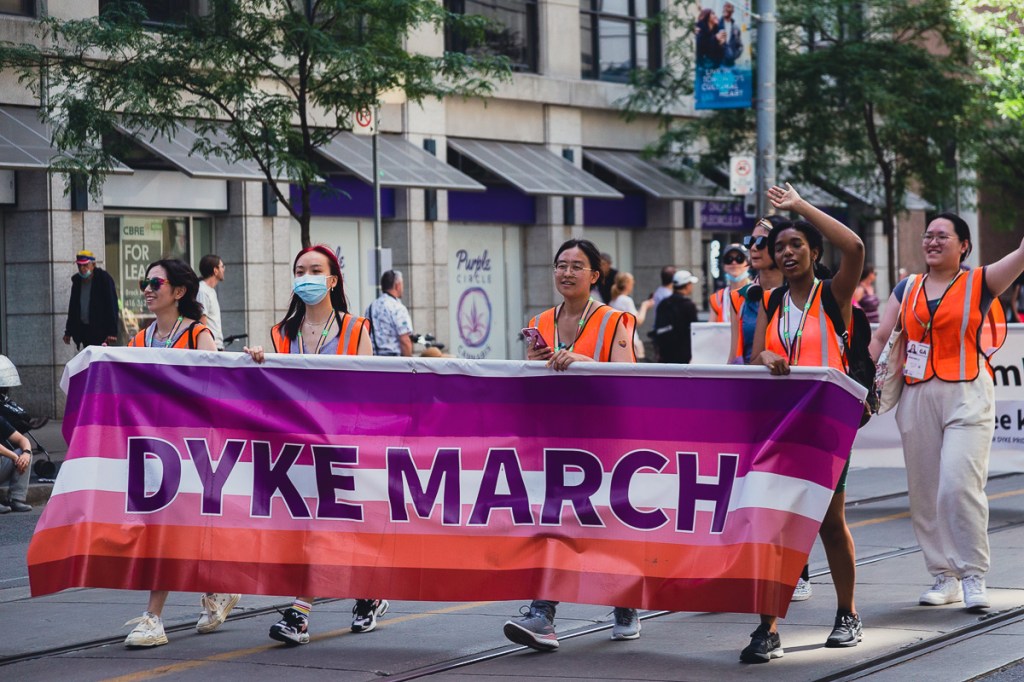 Women walking while carrying a "Dyke March" banner. © Andy Lee, 2022. realandylee.com