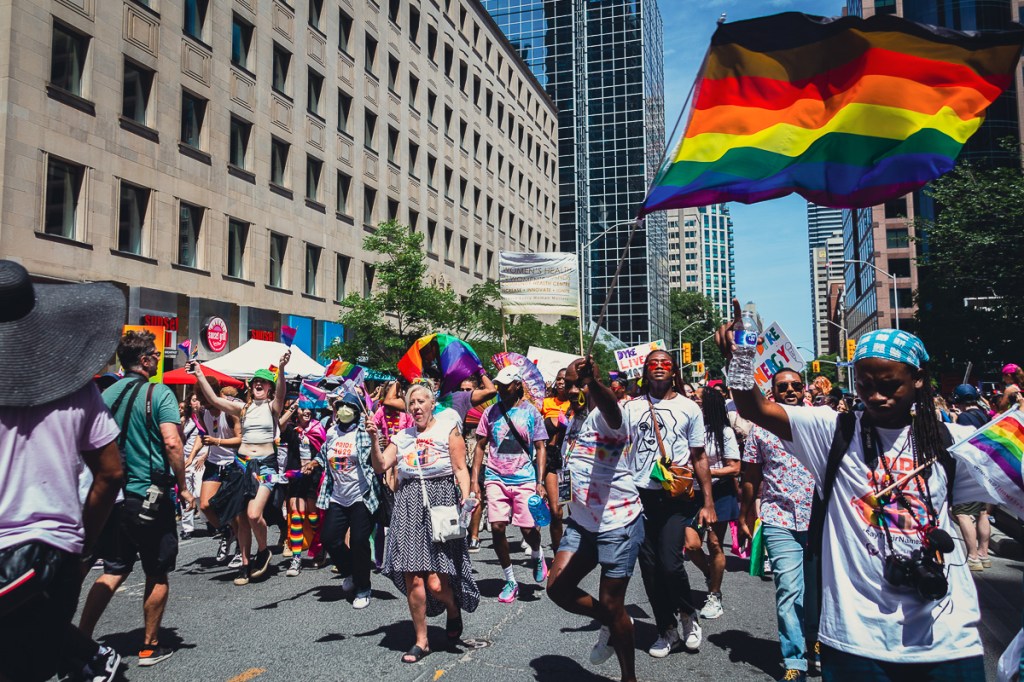 A Black man charges with a rainbow flag during the Dyke March in Toronto. © Andy Lee, 2022. realandylee.com