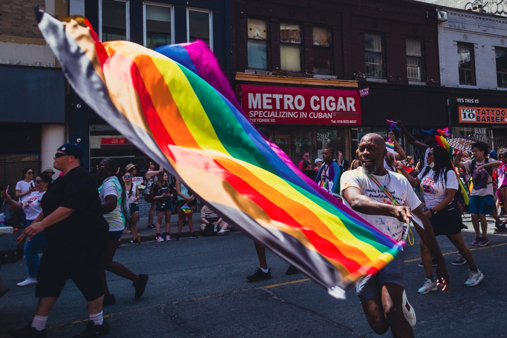 A Black man waves a rainbow flag during the Dyke March in Toronto. © Andy Lee, 2022. realandylee.com