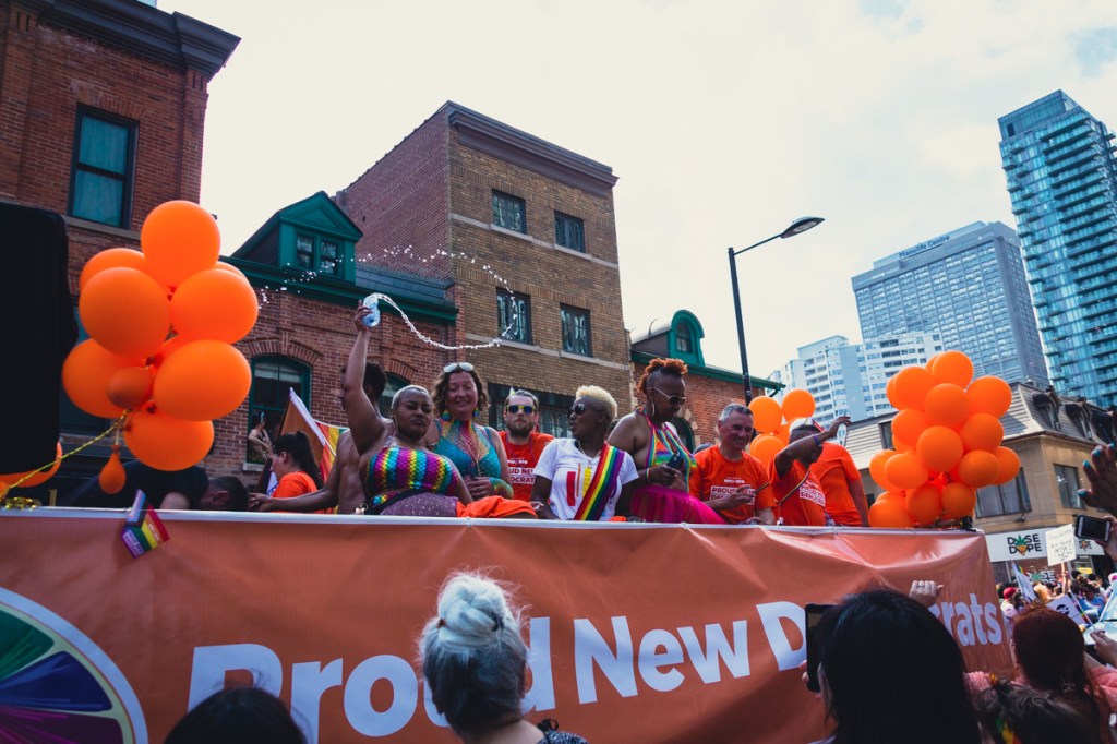 A Black woman splashes water on the crowd from an orange float at the Toronto Pride Parade. © Andy Lee, 2022. realandylee.com