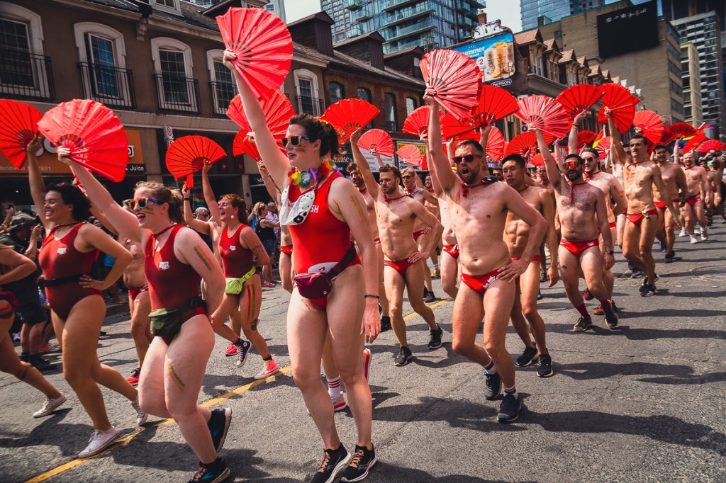 A group of men and women in red swimsuits wave red fans on the street. © Andy Lee, 2022. realandylee.com