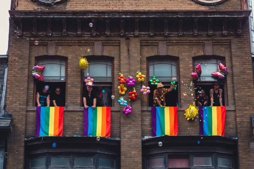 Onlookers watch the Toronto Pride Parade from their second-storey apartment windows, decorated with rainbow flags and balloons. © Andy Lee, 2022. realandylee.com