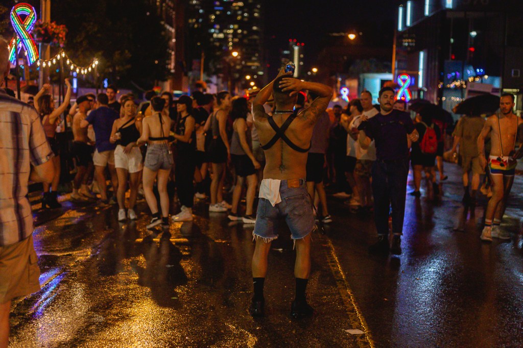 A shirtless man dances in front of a crowd on a wet street at night. © Andy Lee, 2022. realandylee.com