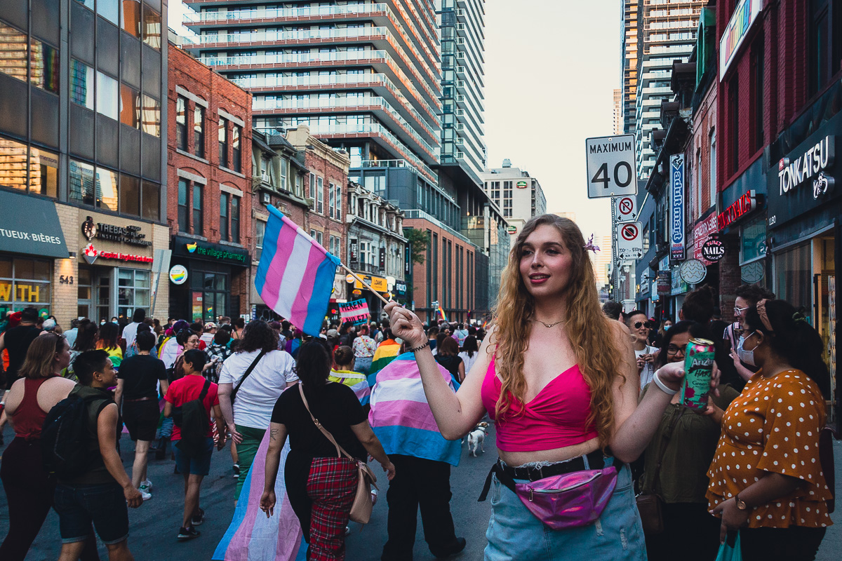 A blonde trans woman waves a blue, pink and white flag during the Trans March in downtown Toronto. © Andy Lee, 2022. realandylee.com