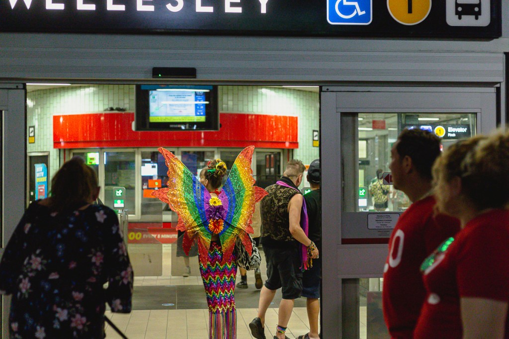 A woman wearing a sparkly rainbow butterfly costume inside Wellesley TTC subway station. © Andy Lee, 2022. realandylee.com