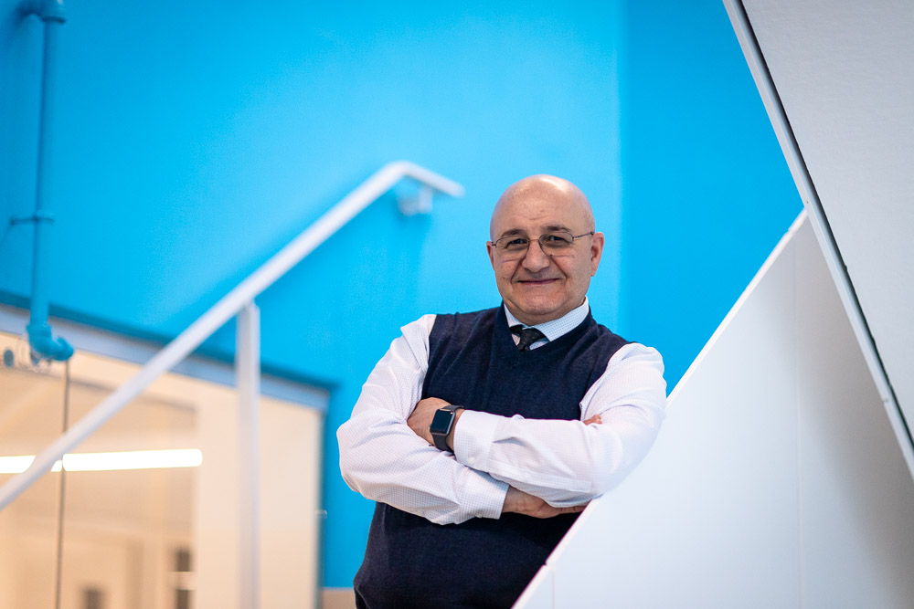 Bald male professor with glasses standing with arms crossed in blue stairwell